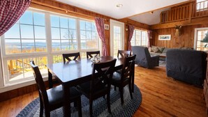 Un interior de madera con una mesa de comedor, sillas, un sofá y ventanas grandes que ofrecen vistas al exterior.