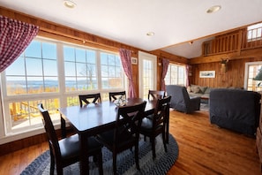 Un interior de madera con una mesa de comedor, sillas, un sofá y ventanas grandes que ofrecen vistas al exterior.