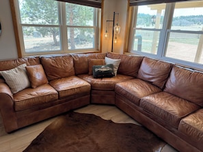 A corner sectional sofa with a leather finish, a shaggy brown rug, and a view of a fenced outdoor area through large windows.
