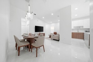 A modern interior with a dining area, a flat-screen TV, and a kitchen. - 4BR Modern Home | Sleeps 14 | BBQ & Outdoor Space (Hialeah)