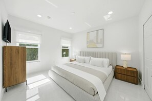 Une chambre moderne avec un grand lit, des tables de chevet, une armoire et un téléviseur fixé au mur.