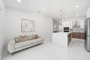 A modern kitchen with white cabinetry, a stainless steel refrigerator, and a built-in oven. - 4BR Modern Home | Sleeps 14 | BBQ & Outdoor Space (Hialeah)