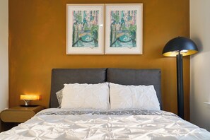 Une chambre d’hôtel avec un lit, une table de chevet avec une lampe et deux tableaux encadrés au mur.