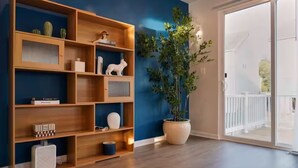 A room with a wooden bookshelf, a potted plant, and a sliding glass door leading to an outdoor area. - Brand-New- Rooftop Luxe 4BR/5BA, 15 Min to DC+ MGM (Upper Marlboro)