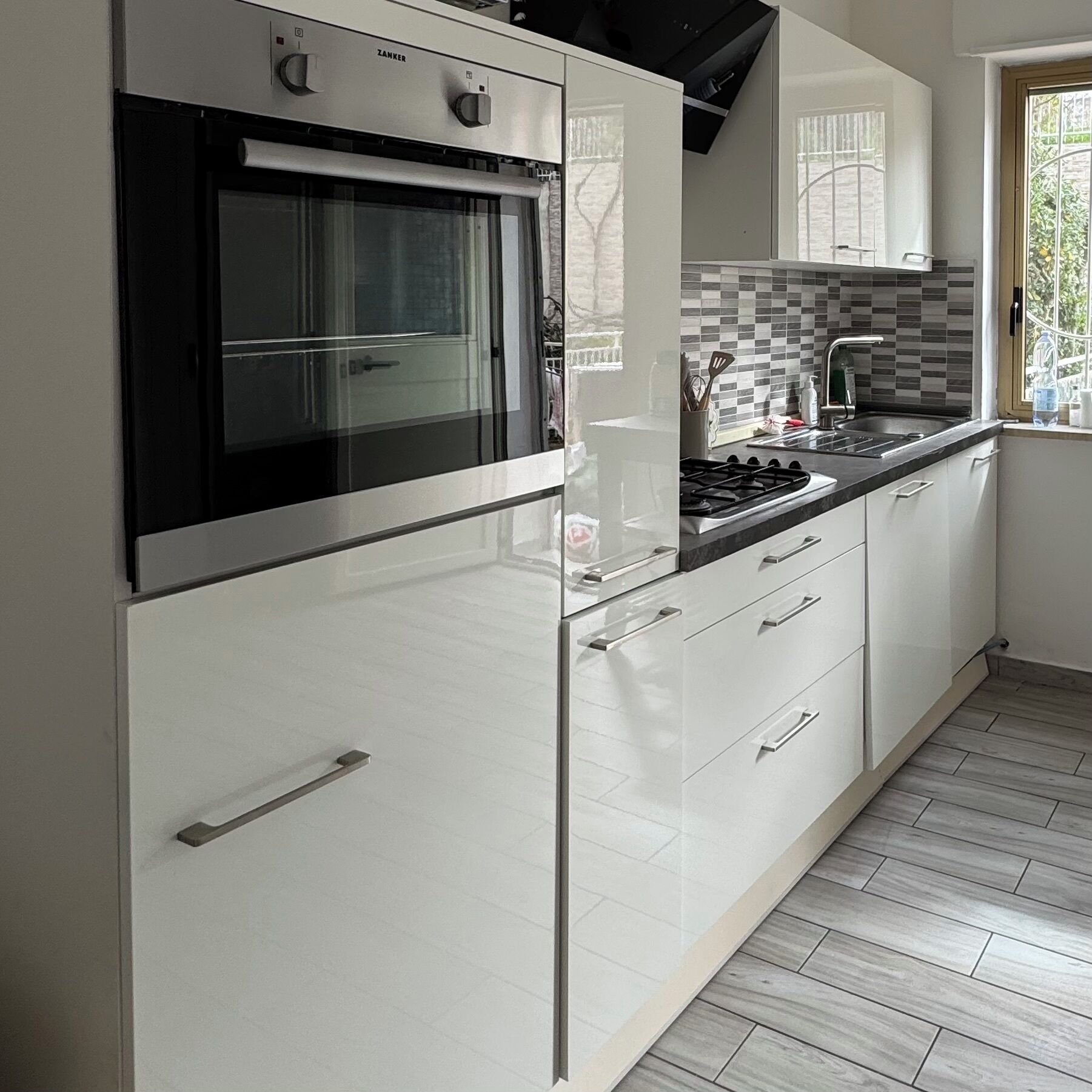 A modern kitchen with a built-in oven, a gas stove, white cabinetry, and a tiled backsplash.