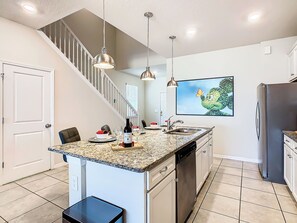 A kitchen with a granite countertop, stainless steel appliances, a dishwasher, and a dining area with chairs and a table. - Dream Home 7BR – Pool, Hot Tub, Game Room & Theater - Near Disney! (Davenport)