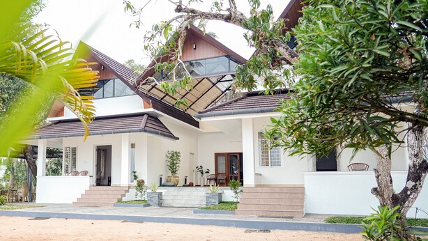 A modern house with a large glass window, a wooden deck, and a staircase leading to the entrance. - River Suite with River View (Kochi)