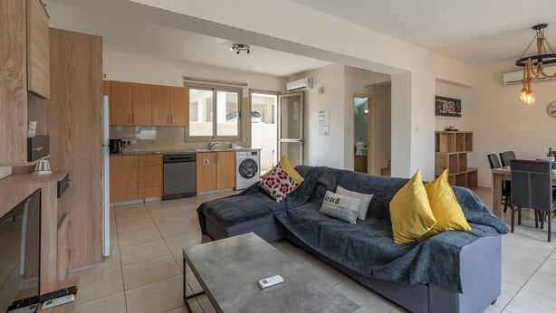 Een moderne woonkamer met een grijze bank, een salontafel, en een eethoek met een tafel en stoelen.