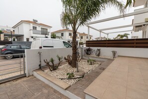 A residential area with a white van parked near a gated entrance, a palm tree, and a small garden with various plants. - 3BR Azure Pearl Seaside Villa, 50 meters from Pernera Beach in Protaras (Paralimni)