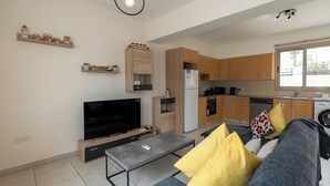 Een moderne woonkamer met een flatscreen televisie, bank, salontafel en een keukenhoek met houten kasten en een koelkast.