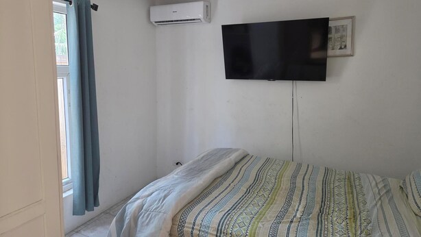 Un dormitorio con cama, un televisor de pantalla plana montado en la pared y un equipo de aire acondicionado.