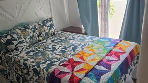 Un dormitorio con cama, cabecera, ventana con cortinas y vistas al exterior.