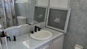 Un baño con lavamanos blanco, inodoro, cortina de ducha con estampado de estrella de mar y un espejo grande.