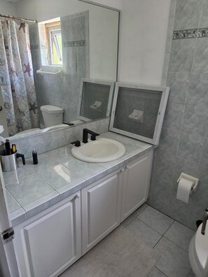Un baño con lavamanos blanco, inodoro, cortina de ducha con estampado de estrella de mar y un espejo grande.