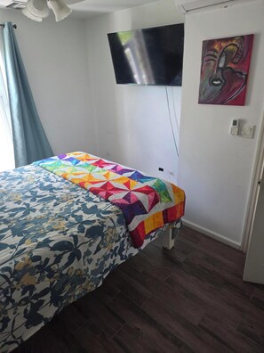 Un dormitorio con una cama, un televisor montado en la pared y un cuadro.