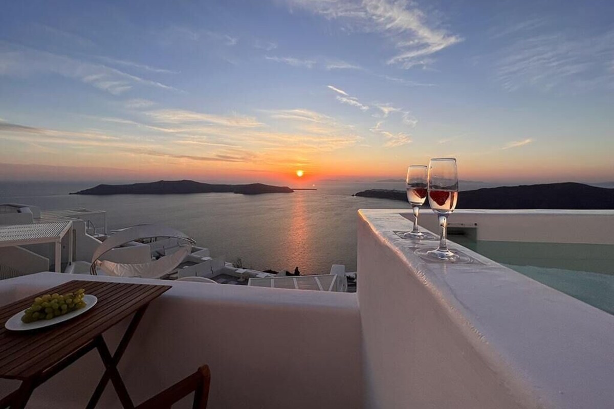 A terrace with a sunset view, two glasses of wine, and a plate of olives.
