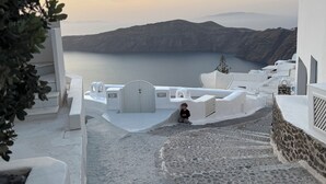 Ein weißes Gebäude mit einer Treppe, die zu einer Terrasse mit Blick auf ein Gewässer und Berge führt.