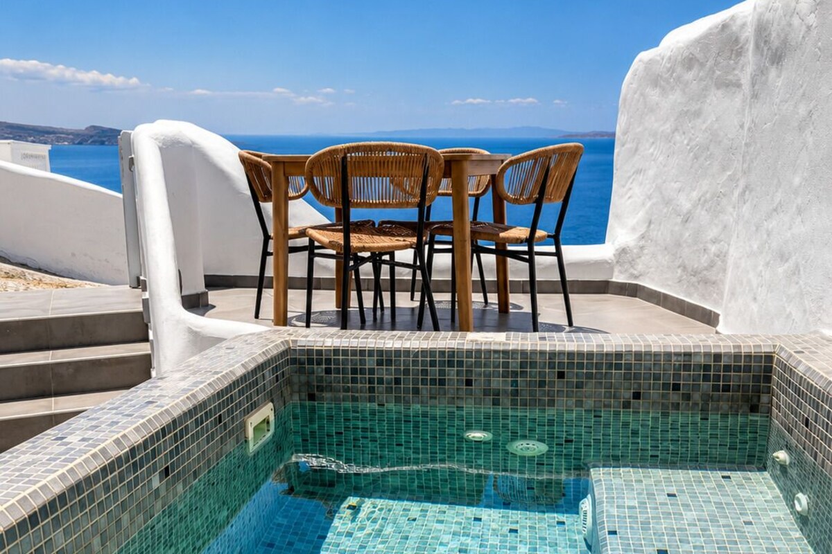 A rooftop pool with mosaic tiles, wooden chairs, and a white wall.