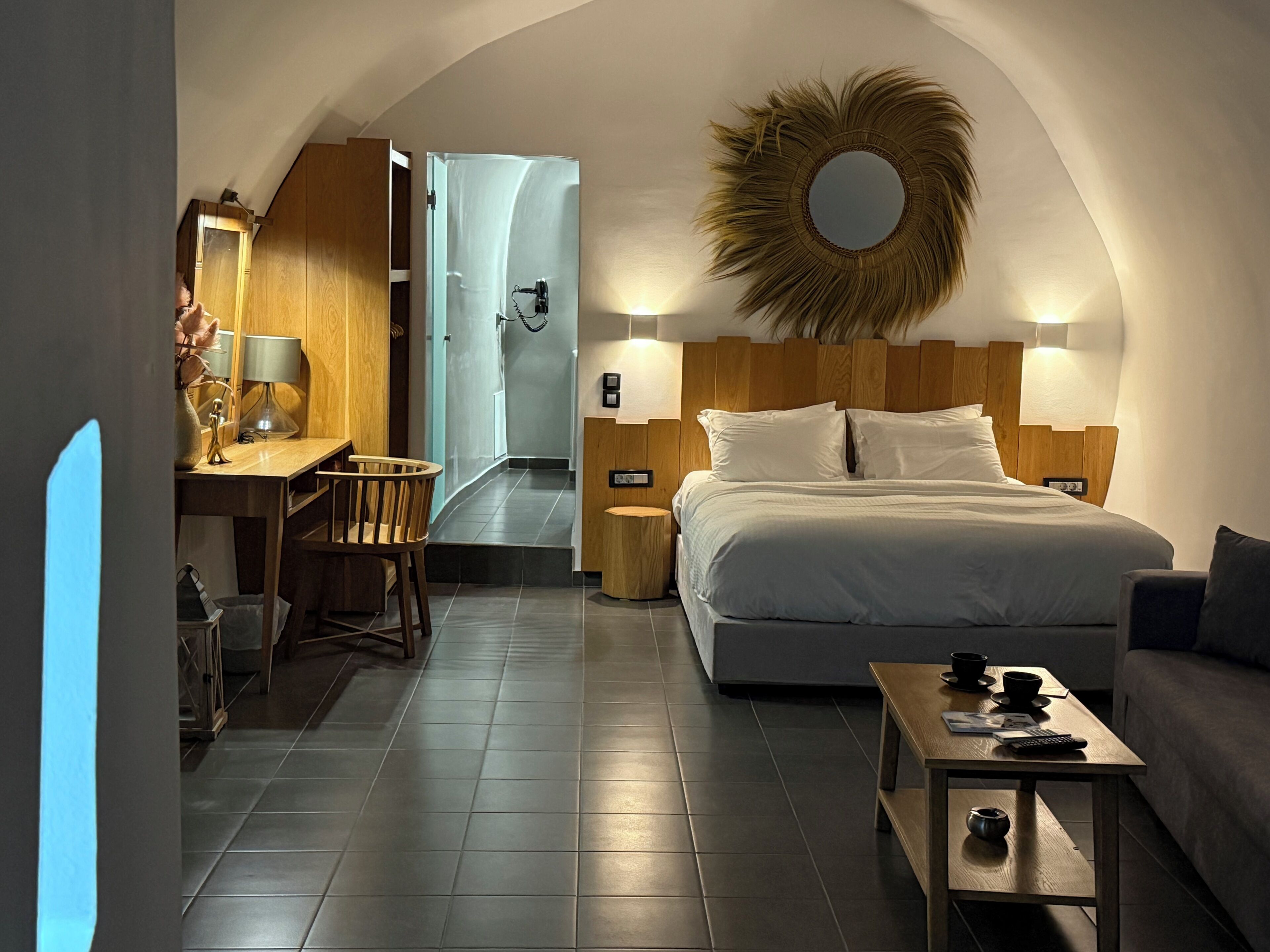 A hotel room with a bed, a desk, a chair, a small table, a sofa, and a shower area.