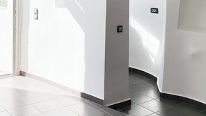 A bright hallway with white walls, a tiled floor, and a door leading outside. - Esmi Suites Santorini (Imerovigli)