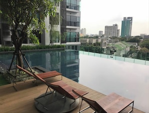 Une piscine à débordement avec des chaises longues, un arbre et une vue sur la ville.