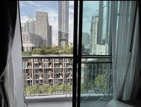 Une pièce dotée d’une grande fenêtre, offrant une vue sur des immeubles de grande hauteur, et d’un balcon avec des balustrades en métal.