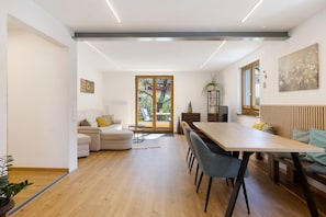 Ein modernes Wohnzimmer mit einer Couch, einem Esstisch und Stühlen. Ein Schiebeglastür führt zu einem Balkon.