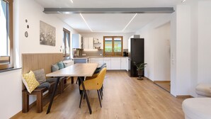 A modern kitchen with a wooden bench and table, a refrigerator, and a window with a view. - Apartment “Am Brändbach” with Private Terrace, Garden, and Wi-Fi (Bräunlingen)