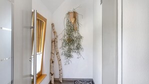 A narrow hallway with a wooden door, a window with blinds, a patterned mat, and a hanging plant. - Apartment “Am Brändbach” with Private Terrace, Garden, and Wi-Fi (Bräunlingen)