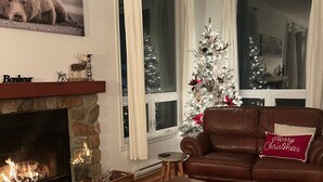 A living room with a fireplace, a Christmas tree, a brown leather sofa, and a coffee table. - Chalet La Félicita, enchanting waterfront. (Saint-Adolphe-d'Howard)