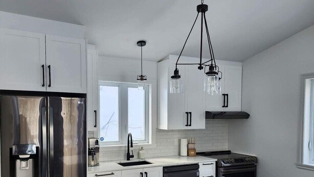 A modern kitchen with a stainless steel refrigerator, a central island with bar stools, and pendant lighting. - Chalet La Félicita, enchanting waterfront. (Saint-Adolphe-d'Howard)