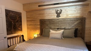 A wooden-paneled room with a bed, a mounted deer head, and a painting on the wall. - Chalet La Félicita, enchanting waterfront. (Saint-Adolphe-d'Howard)