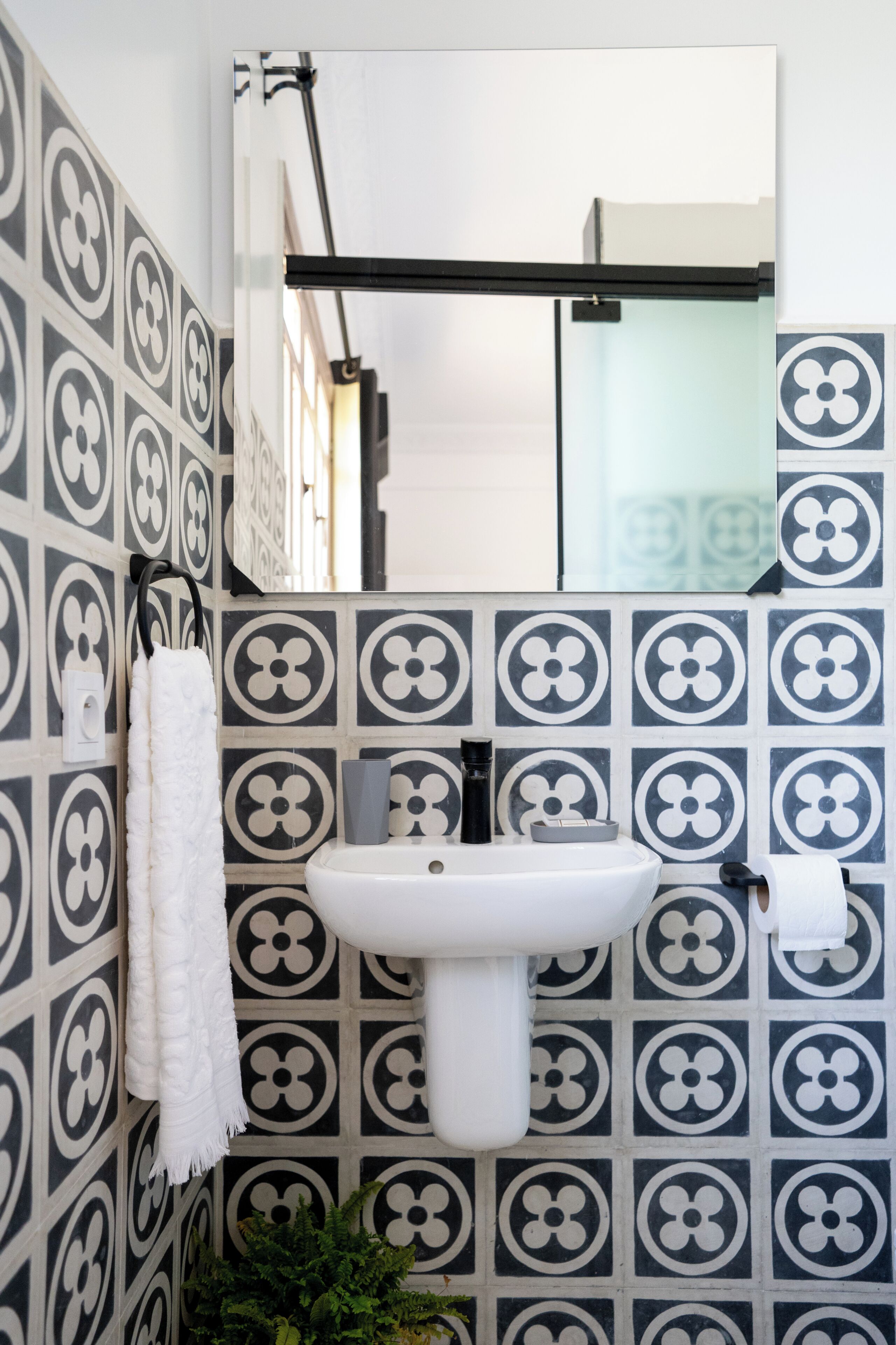 Un baño con un lavamanos blanco, baldosas con estampado blanco y negro, una toalla blanca y un espejo.