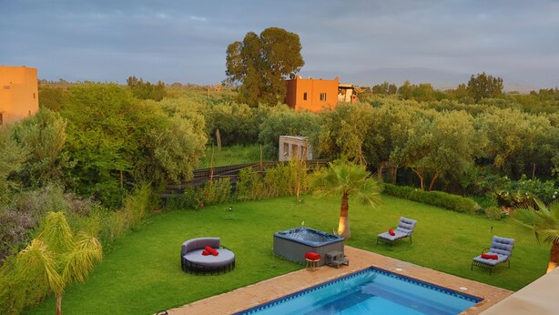 En swimmingpool med liggestole og jacuzzi i en frodig have.