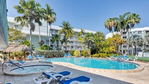 A pool area with lounge chairs, a hot tub, and palm trees. - Vitamin Sea at LaBrisa - Oceanfront View! (Key West)