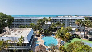 Um hotel com piscina, palmeiras e vista para o oceano.