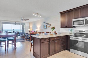 A modern kitchen with dark wood cabinets, a stainless steel microwave, and an oven. There's a dining area with a table and chairs, and a view of the ocean through large windows. - Vitamin Sea at LaBrisa - Oceanfront View! (Key West)