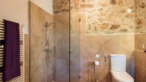 A bathroom with a glass-enclosed shower, a toilet, and a stone wall. - Ayurvila Wellness Retreat: 1-bedroom apartment (Manacor)