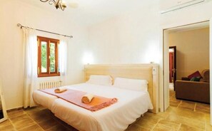Ein Schlafzimmer mit Bett, einem Fenster mit Vorhängen, einem Heizkörper und einer Tür zu einem anderen Raum.