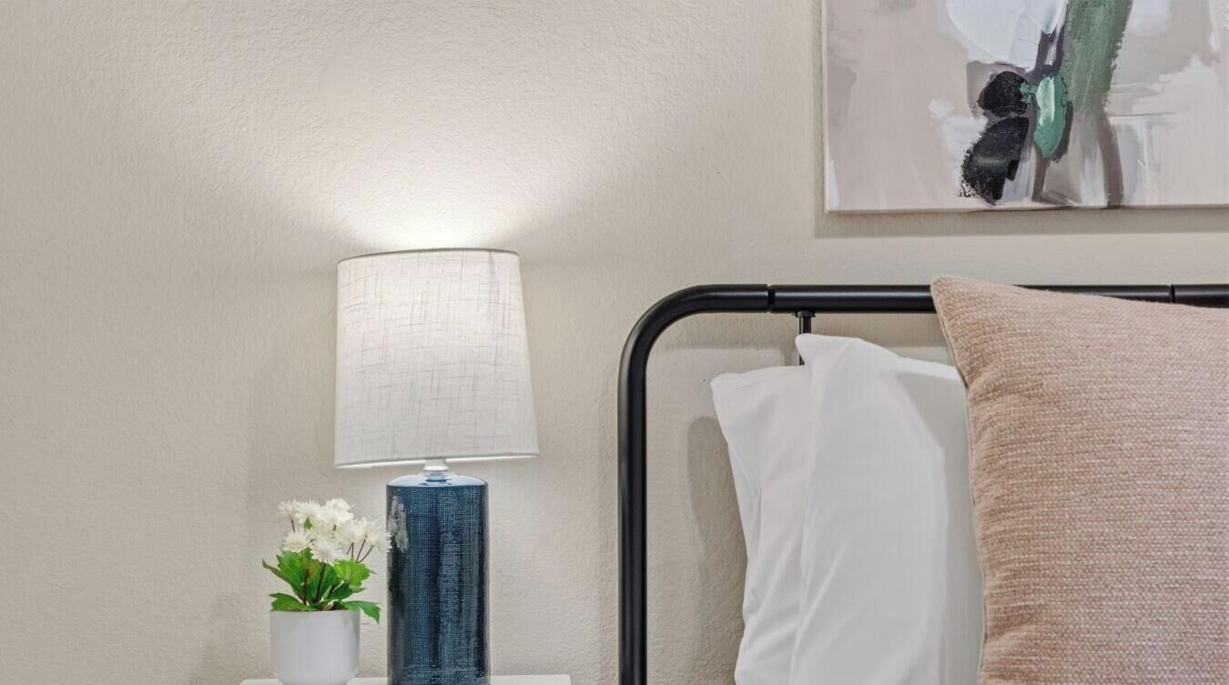 Une chambre d’hôtel bien rangée, avec un lit, une lampe de chevet, un vase de fleurs et un tableau au mur.