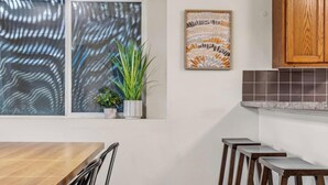 Een keuken met een raam, een plant, een lijst met kunstwerk en een houten kast.