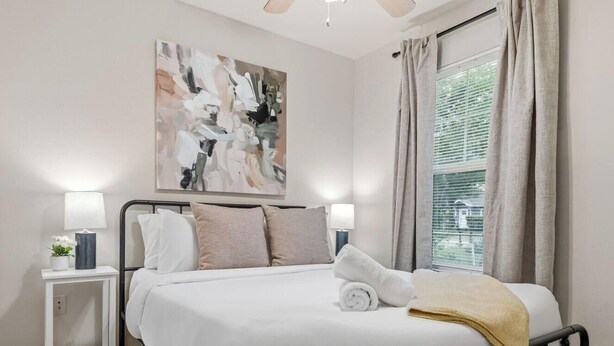 Een hotelkamer met een bed, nachtlampjes, een schilderij en een raam met gordijnen.