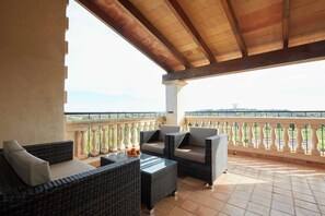 Un espace extérieur aménagé, abrité et doté de mobilier en osier et d’une table en verre, offrant une vue imprenable sur un paysage magnifique.