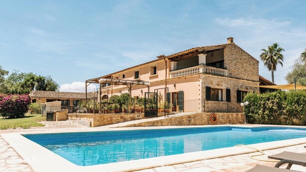 Ein zweistöckiges Haus mit Swimmingpool, Steinmauern und einem Balkon.