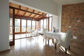 A dining area with a table and chairs, a stone wall, and a view of the outdoors. - Serene Mallorca Sanctuary for Yoga Retreats & Events (Manacor)