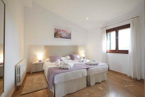 Une chambre d’hôtel avec deux lits, un radiateur, un tableau, une fenêtre avec des rideaux et une table de chevet avec une lampe.