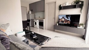 A modern living room with a sofa, coffee table, and a flat-screen TV mounted on a wall. - Luxury Condo in Khlong Toei City Views & Skytrain Access (Bangkok)