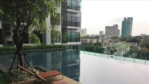 A modern building with a rooftop pool, lounge chairs, and a tree. - Luxury Condo in Khlong Toei City Views & Skytrain Access (Bangkok)