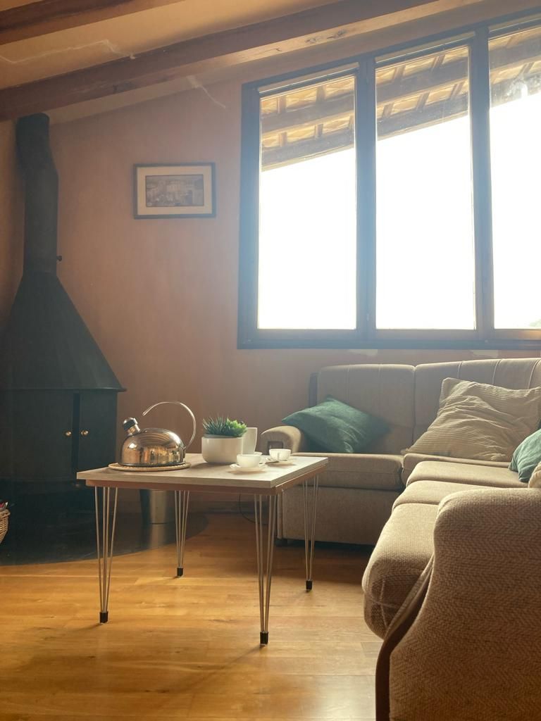 Uma sala de estar aconchegante com um sofá, uma mesa com chaleira e uma lareira.