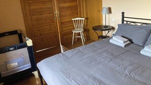 A bedroom with a bed, a chair, a small table with a lamp, and a wooden wardrobe. - El Xiprer - El Refugi de la Vall de Biert Total disconnection 25 min from Girona (CANET D'ADRI)